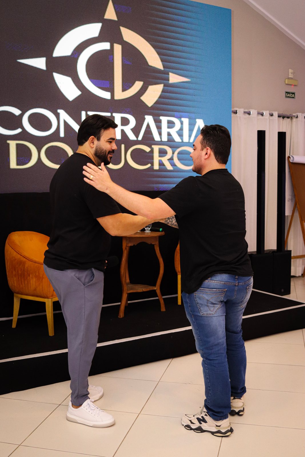 Participantes se abraçando no backdrop da Confraria do Lucro