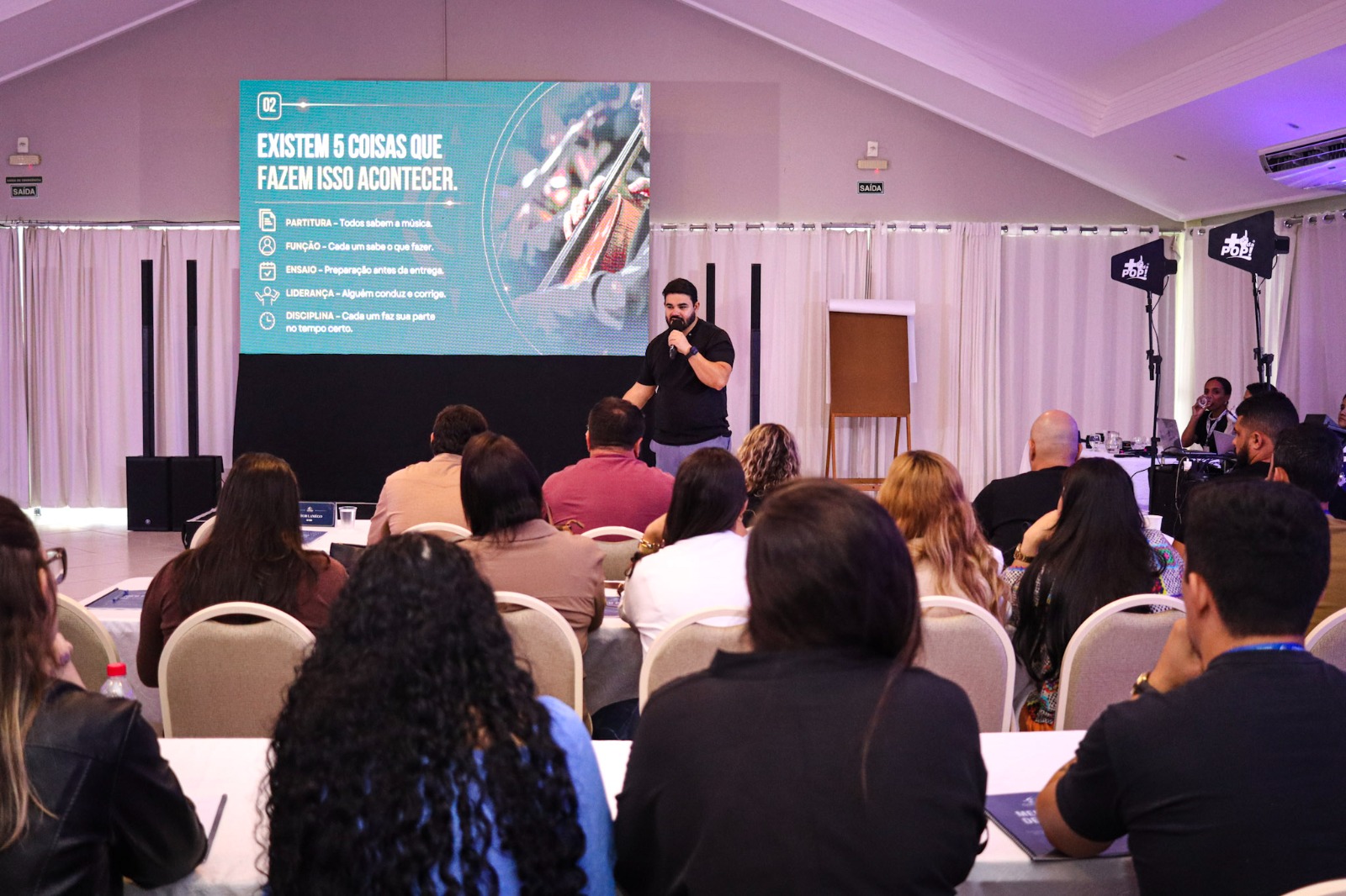 Diego palestrando para uma plateia em um salão de eventos
